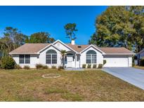 Charming single-story white home with a well-manicured front yard and attached garage at 8231 Sw 108Th Loop, Ocala, FL 34481