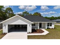 Charming white single story house with an attached two car garage, manicured lawn, and dark gray roof at 8295 Se 159Th Ln, Summerfield, FL 34491