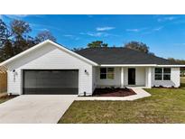 Charming single-story home with a two-car garage, green lawn and modern black and white color scheme at 8295 Se 159Th Ln, Summerfield, FL 34491