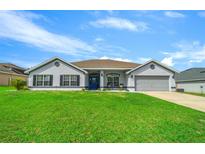 Charming one-story home with lush green lawn and a blue front door with a gray exterior and two car garage at 6875 Se 11Th Pl, Ocala, FL 34472