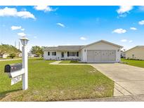 Well-maintained single-story home with a green lawn and a two-car garage featuring a large driveway on a beautiful sunny day at 17421 Se 107Th Ct, Summerfield, FL 34491