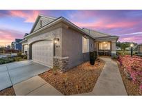 Charming exterior view of home featuring a two-car garage, stone accents, and manicured landscaping at dusk at 9839 Sw 99Th Loop, Ocala, FL 34481