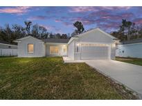 Charming single-story home boasts a manicured lawn, attached garage, and modern architectural design at dusk at 12882 Se 42Nd Ct, Belleview, FL 34420