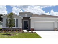 Charming single-story home with a manicured lawn, gray stucco, stone accents, and attached two car garage at 3071 Canopy Oak Blvd, Wildwood, FL 34785