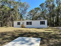 Charming manufactured home featuring white siding, dark shutters, and a serene wooded surrounding at 1921 Nw 120Th Ave, Ocala, FL 34482