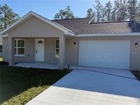 Front exterior featuring a two-car garage, a light-colored stucco finish, and a well-manicured lawn at 127 Sw Alvarez Rd, Dunnellon, FL 34431