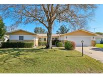 Charming home featuring a manicured lawn, mature tree, and an attached two-car garage at 9305 Bahia Track Way, Ocala, FL 34472