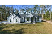 Stylish single-story home featuring crisp white exterior, dark gray roof, and lush green lawn at 13751 Sw 49Th Pl, Ocala, FL 34481