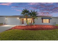 Charming home exterior with manicured lawn, colorful mulch, and young palm trees at dusk at 2013 Cardona Way, The Villages, FL 32159