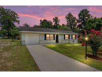 Charming one-story home with brick accents, green lawn, and lovely landscaping at sunset at 23 Juniper Pass Ln, Ocala, FL 34480