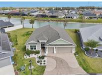 Beautiful lakefront property with lush landscaping and a spacious driveway with a decorative concrete design at 5766 Henry Loop, The Villages, FL 32163