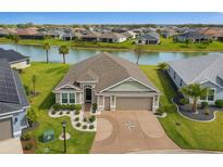 Beautiful home featuring a tranquil pond view, well-manicured lawn, and a spacious driveway with a unique compass design at 5766 Henry Loop, The Villages, FL 32163