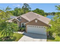 An exterior view of a tan home featuring a two-car garage, manicured lawn, and scenic lake backdrop at 1201 Creekview Ct, St Cloud, FL 34772