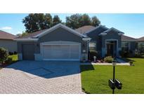 Charming home featuring a gray exterior, well-maintained lawn, and a stylish brick driveway at 13968 Se 96Th Cir, Summerfield, FL 34491