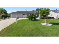 Well-maintained single-story home boasts a lush green lawn, mature landscaping, and attached two-car garage at 1482 Abercrombie Way, The Villages, FL 32162