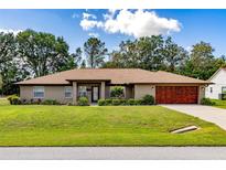 Charming single-story home featuring a manicured lawn and a stylish, wood-look garage door at 5770 Sw 89Th Pl, Ocala, FL 34476