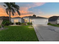 Charming single-story home with manicured lawn, mature palm tree, and two-car garage, bathed in the warm glow of sunset at 680 Farmington Ave, The Villages, FL 32162
