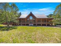 Stunning log cabin home with a metal roof and a large front porch, set against a backdrop of lush greenery at 3360 Se 183Rd Avenue Rd, Ocklawaha, FL 32179