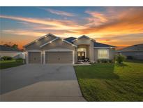 Inviting home exterior featuring a well-manicured lawn and a two-car garage against a breathtaking sunset sky at 9074 Se 48Th Court Rd, Ocala, FL 34480