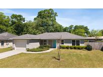 Charming single-story home with a well-manicured lawn, lovely landscaping, and a bright turquoise front door at 5591 Nw 57Th Pl, Ocala, FL 34482