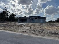 Unfinished single-story home with gray siding, a front yard covered with sand, and a cloudy sky at 4424 Sw Carnation Ct, Dunnellon, FL 34431