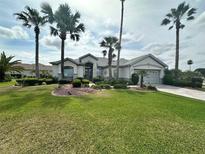 Beautiful single-story home featuring a well-manicured lawn, lush landscaping, and stately palm trees at 12453 Se 93Rd Court Rd, Summerfield, FL 34491