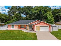 Charming coral home featuring a well-manicured lawn, attached garage, and stone accents at 1109 Ne 22Nd Ave, Ocala, FL 34470