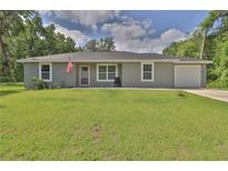 Charming single-story home with a well-manicured lawn, an American flag, and a gray exterior at 838 Nw 124Th Street, Citra, FL 32113