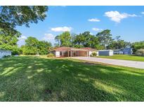Spacious front yard with a well-maintained lawn and a house featuring a carport and long driveway on a sunny day at 10140 Sw 81St Terrace Rd, Ocala, FL 34481
