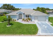 Charming single-story home with light blue exterior, well-manicured lawn and a two car garage on a sunny day at 17755 Se 117Th Cir, Summerfield, FL 34491