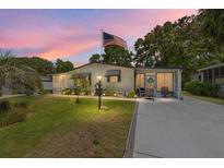 Charming single-story home featuring a well-manicured lawn, cozy porch and an American flag at sunset at 514 Saint Andrews Blvd, Lady Lake, FL 32159