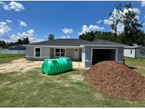 Single Gathering home showcasing its gray exterior, attached garage, green septic tank, and pile of mulch in yard at 1057 Nw 68Th Pl, Ocala, FL 34474