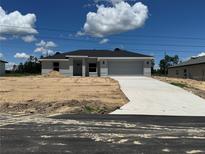 New construction home with a gray facade, a two-car garage, and a concrete driveway in a partially landscaped yard at 15419 Sw 65Th Terrace Rd, Ocala, FL 34473