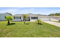 Charming home featuring a well-maintained lawn, an attached two-car garage, and beautiful landscaping with lovely palm trees at 8849 Sw 116Th Place Rd, Ocala, FL 34481