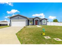 Inviting single-story home featuring a two-car garage, well-maintained lawn, and a red front door at 10291 Se 67Th Ter, Belleview, FL 34420