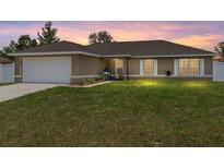 Charming single-story home with a well-manicured lawn and a two-car garage at sunset at 3887 Sw 156Th Pl, Ocala, FL 34473