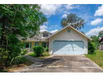 Charming single-Gathering home featuring a light yellow exterior, light blue trim and a two-car garage with a concrete driveway at 8 Juniper Pass Way, Ocala, FL 34480
