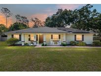 Charming single-story home featuring a metal roof, solar panels, rocking chairs on the porch, and a lush green lawn at 1601 Ne 47Th Ct, Ocala, FL 34470