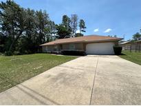Single-story home with a well-maintained lawn, mature trees, and a large driveway leading to a two-car garage at 7800 Sw 127Th Loop, Ocala, FL 34473