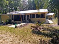 Charming home with yellow siding, metal roof, and a large screened-in porch, nestled among mature trees and landscaping at 22736 Sw 117Th St, Dunnellon, FL 34431