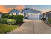 Charming single-story home with a two-car garage, lush landscaping, and a concrete driveway, set against a colorful sunset at 2296 Sheehan St, The Villages, FL 32163