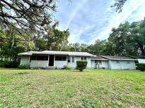 Charming single-story home with a light blue exterior, a screened porch, and a metal roof surrounded by lush greenery at 2409 Nw 7Th St, Ocala, FL 34475
