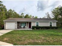 Charming single-story home with a well-manicured lawn, a red front door and an attached one car garage at 120 Fisher Ct, Ocklawaha, FL 32179