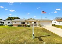 Charming single-story home featuring a well-manicured lawn, white siding, and an American flag in a sunny neighborhood at 17890 Se 96Th Ct, Summerfield, FL 34491