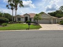 Charming single-story home with a well-manicured lawn, mature palm trees, and a brick-paved driveway at 9459 Se 124Th Loop, Summerfield, FL 34491