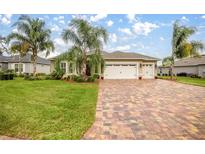 Beautiful single-story home with mature landscaping, brick driveway, and a three-car garage at 10279 Julia Isles Ave, Oxford, FL 34484