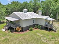 Secluded home with a metal roof, charming porch, and steps leading to the landscaped yard at 12080 Se Sunset Harbor Rd, Weirsdale, FL 32195