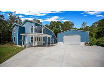 Inviting blue two-story home with a covered front porch, a large garage, and a concrete driveway at 12690 Ne Highway 315, Fort Mc Coy, FL 32134