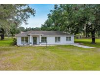 Charming one-story home with white exterior, well-maintained lawn, and mature trees on a sunny day at 6350 Nw 135Th Ave, Morriston, FL 32668