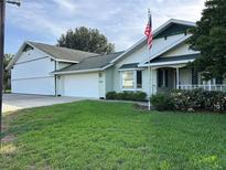 Charming single-story home with a lush green lawn and a three car garage with an American flag at 9622 Se 71St Ct, Ocala, FL 34472